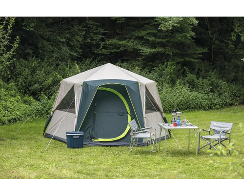 Campingzelt mit Campingmöbeln auf einer Wiese vor Bäumen