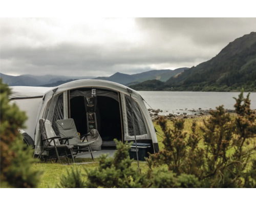 Campingplatz mit Zelt, Campingstühlen und Kühlbox am See mit Bergen im Hintergrund