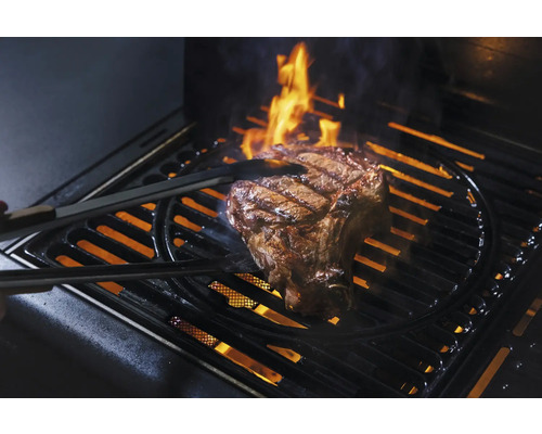 Ein Steak wird mit einer Zange auf einem Grill gegrillt, Flammen sind zu sehen.