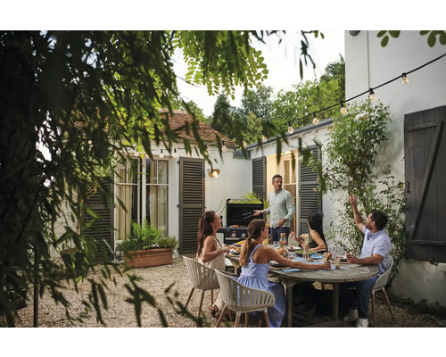 Gesellige Gartenszene mit Grill, Esstisch und Gartenbeleuchtung für ein entspanntes Ambiente.