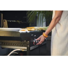 Eine Person bedient einen Campingaz Gasgrill mit darauf liegenden Speisen.