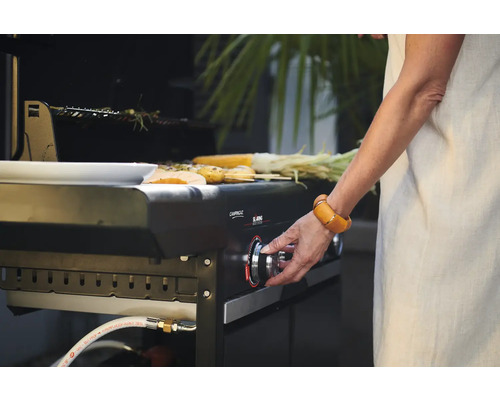 Eine Person bedient einen Campingaz Gasgrill mit darauf liegenden Speisen.