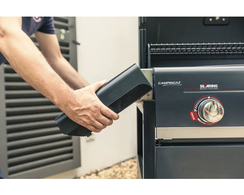 Eine Person setzt eine Powerbox in einen Gasgrill von Campingaz ein.