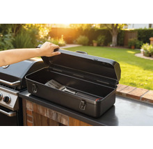 Geöffnete Grillbesteckkiste mit Grillwender neben Grill im Garten.