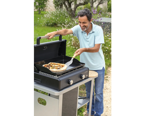 Mann bereitet Pizza auf einem CampinGaz Grill im Garten zu.