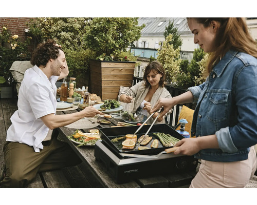 Personen grillen Gemüse auf einem Tischgrill im Freien bei einer Gartenparty.