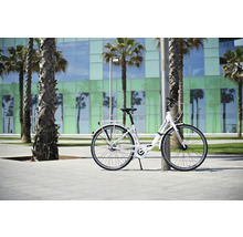 Weißes Cityrad lehnt an einem Pfosten vor Palmen und einem Gebäude.