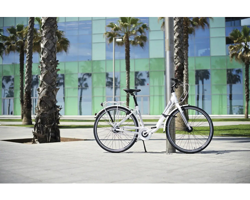 Weißes Cityrad lehnt an einem Pfosten vor Palmen und einem Gebäude.