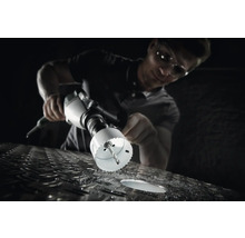 Ein Mann bohrt mit einer Lochsäge ein Loch in eine Metalloberfläche.