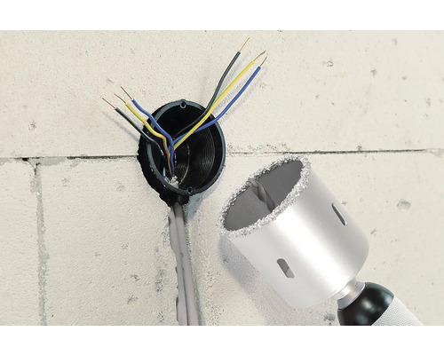 Wand mit Bohrloch, Elektrokabeln und einer Bohrkrone.