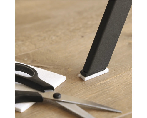 Stuhlbein mit Filzgleiter, Filzgleiter und Schere auf Holzboden