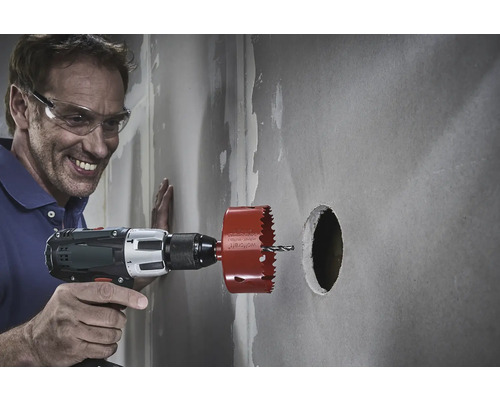 Ein Mann mit Schutzbrille bohrt mit einer Lochsäge ein Loch in eine Wand.