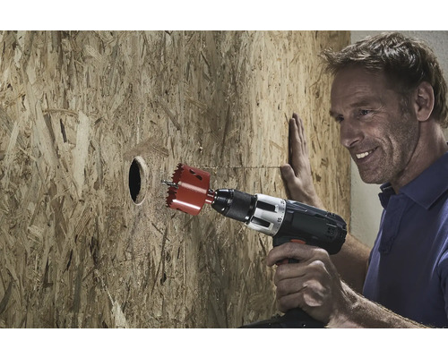 Mann bohrt mit einer Lochsäge ein Loch in eine Holzplatte