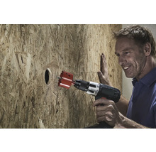 Mann bohrt mit einer Lochsäge ein Loch in eine Holzplatte