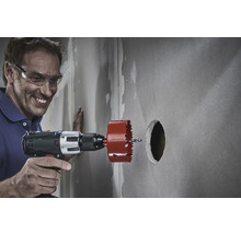 Ein Mann bohrt mit einer Lochsäge ein Loch in eine Wand.