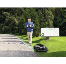 Mann steuert Mähroboter mit Smartphone im Garten