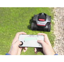 Person bedient einen Rasenmähroboter per Smartphone-App im Garten