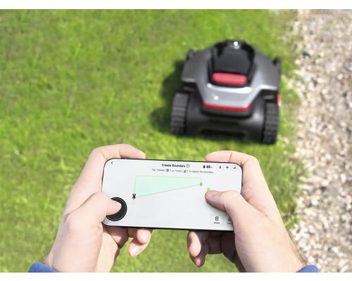 Person bedient einen Rasenmähroboter per Smartphone-App im Garten