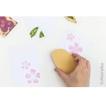 Hand, die mit Stempel und Stempelkissen ein florales Muster auf Papier druckt
