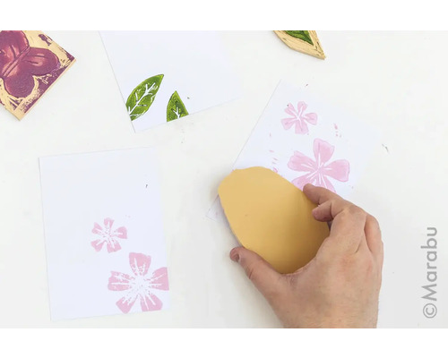 Hand, die mit Stempel und Stempelkissen ein florales Muster auf Papier druckt