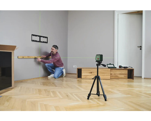 Mann benutzt Laser-Wasserwaage zum Ausrichten eines Regals an einer Wand