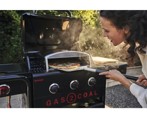 Frau schiebt Pizza mit Pizzaschieber in Gasgrill mit Pizzaofenaufsatz