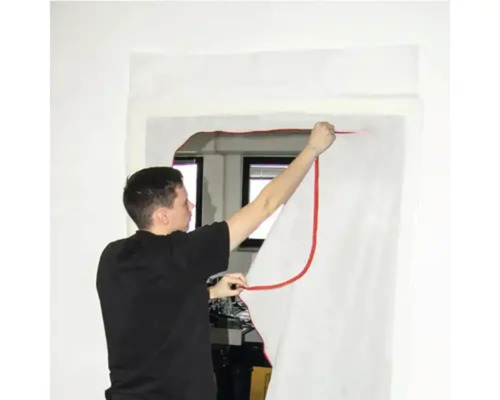 Eine Person verwendet eine Dichtfolie, um eine Tür abzudichten.