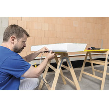 Mann befestigt Dichtband an einer Dämmplatte auf einer Arbeitsbockkonstruktion.