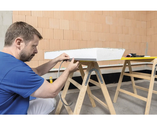Mann befestigt Dichtband an einer Dämmplatte auf einer Werkbank.