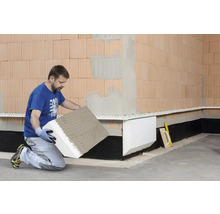 Ein Mann kniet und befestigt eine Dämmplatte an einer Wand.