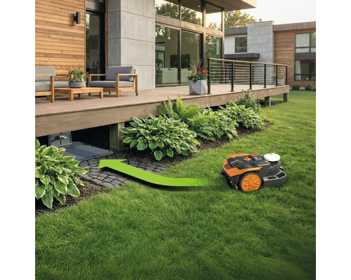 Ein Rasenmähroboter fährt mit einem grünen Pfeil zu seiner Ladestation unter einer Terrasse.