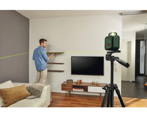 Mann montiert Regale mit einem Bosch Kreuzlinienlaser auf einem Stativ in einem Wohnzimmer