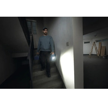 Mann geht Treppe runter mit Werkzeugkoffer und Arbeitsleuchte in der Hand