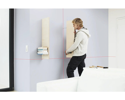 Mann montiert ein Wandregal mit einem Laser