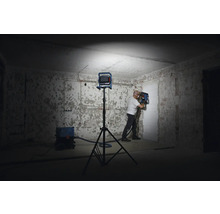 Mann arbeitet mit einer Mauernutfräse in einem Raum, beleuchtet von einem Stativscheinwerfer. Ein Staubsauger steht im Hintergrund.