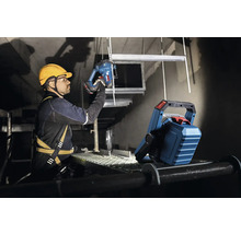 Ein Handwerker mit Schutzhelm und Sicherheitsgurt arbeitet mit einer Stichsäge im Scheinwerferlicht.