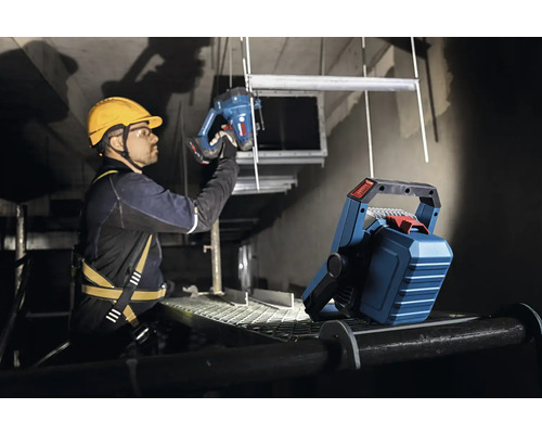 Ein Handwerker mit Schutzhelm und Sicherheitsgurt arbeitet mit einer Stichsäge im Scheinwerferlicht.