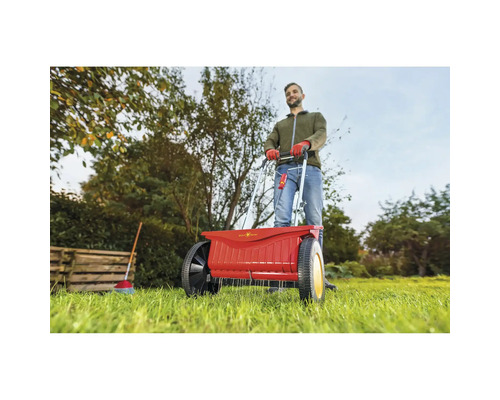 Eine Person bedient einen Düngerstreuer im Garten.