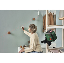 Frau markiert mit einem Laser-Nivelliergerät eine Linie an einer Wand für die Befestigung von Wandhaken