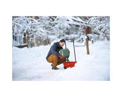 Mann befüllt Streuwagen im Winter mit Streugut