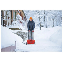 Frau benutzt einen Streuwagen für den Winterdienst auf einem verschneiten Gehweg.