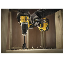 Eine Person bohrt mit einem gelben Akku-Bohrschrauber von DeWalt ein Loch in ein Holzstück.