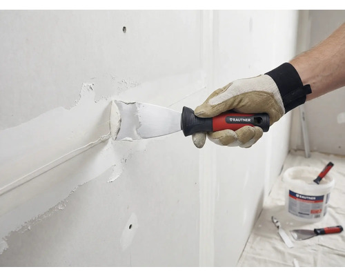 Handwerker spachtelt Wand mit Spachtel und Spachtelmasse. Rautner Logo sichtbar.