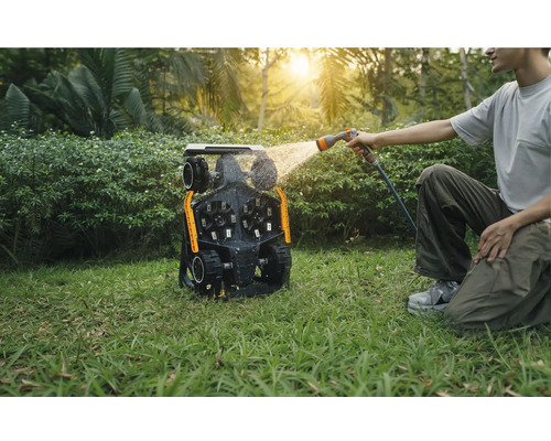Mann reinigt einen Mähroboter mit einem Wasserschlauch im Garten.
