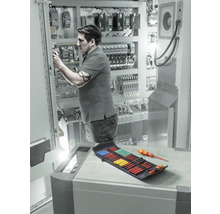 Elektriker arbeitet an Schaltschrank mit Schraubendreher-Set in der Nähe