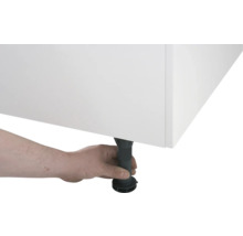 Eine Hand justiert einen schwarzen, höhenverstellbaren Möbelfuß unter einem weißen Schrank.