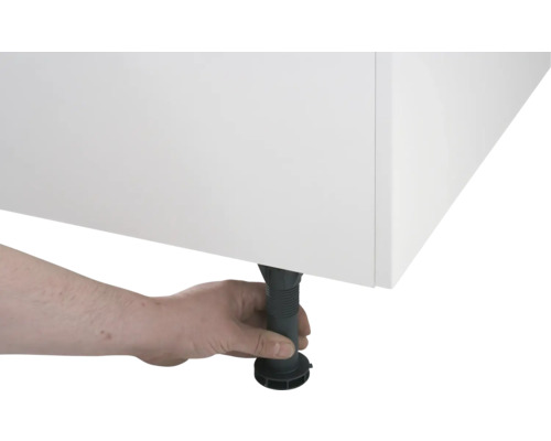 Eine Hand justiert einen schwarzen, höhenverstellbaren Möbelfuß unter einem weißen Schrank.