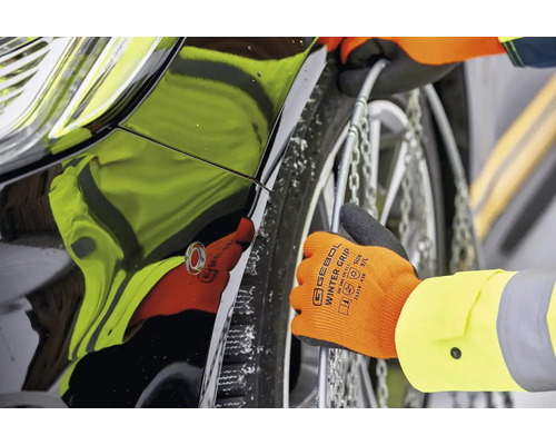 Montage von Schneeketten am Reifen eines Autos mit Handschuhen.