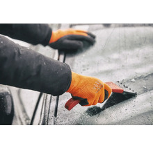 Person mit Handschuhen benutzt einen Eiskratzer an einer Windschutzscheibe