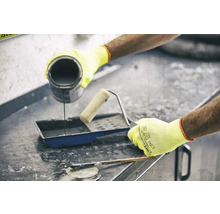 Eine Person gießt Farbe in eine Farbwanne neben einer Farbrolle und einem Spachtel